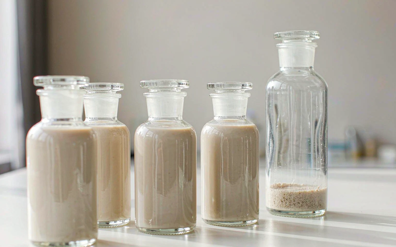 A row of clear sample bottles holding protein drinks at different pH levels, with sediment settled in the base of one bottle