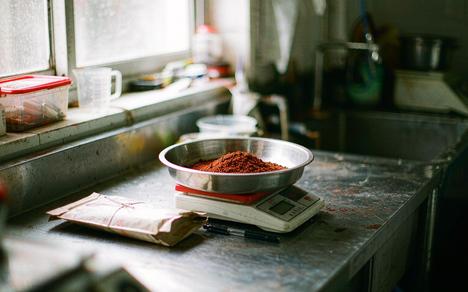 A sample of red brown grape seed extract powder being weighed on a digital scale beside a folded paper sample bag